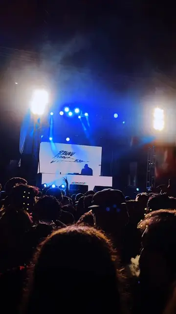 Público de costas diante do palco iluminado em azul, com o nome Bruno Lopes no telão